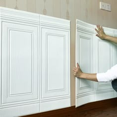 a man kneeling on the floor next to a wall with white cupboards and drawers