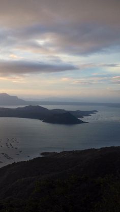 the sun is setting over an island in the ocean with hills and trees on either side