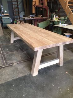 a wooden table sitting in a garage next to a stair case and some other workbench