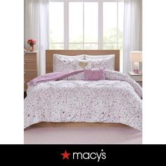 a white bed with pink and purple comforter set on top of it in front of a window