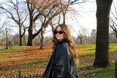 a woman wearing sunglasses and a black leather jacket standing next to a fence in a park