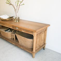 a wooden table with baskets underneath it next to a vase and book on the shelf