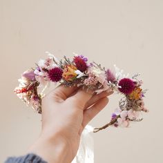 a person holding flowers in their hand with pink and purple flowers on the top of it