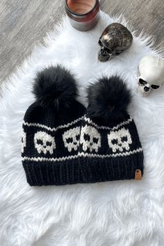 a knitted skull hat with two pom - poms sits on a white fur rug