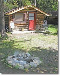 a small log cabin in the woods with a fire pit and picnic table next to it