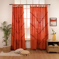 an orange curtain in front of a window next to a wooden table and potted plant