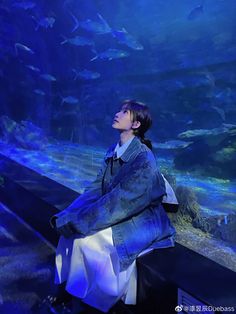 a woman sitting on a bench in front of an aquarium filled with fish and looking up at the sky