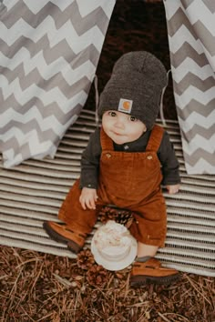 a baby sitting on the ground wearing overalls and a hat