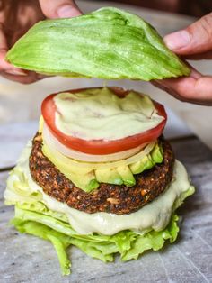 a hamburger with lettuce, tomato and cheese is being held up by someone's hands