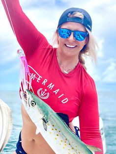 a woman holding a fish in her right hand and wearing sunglasses on the other side