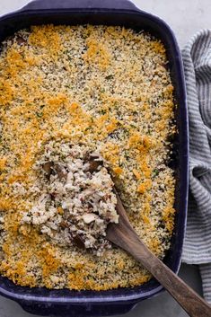 a blue casserole dish filled with cheese and other toppings next to a wooden spoon