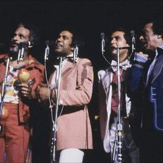 the four men are singing into microphones