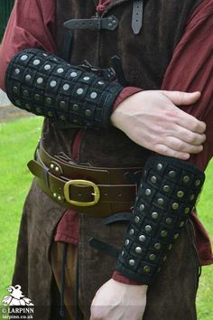 a man wearing leather armor and holding his arm in one hand with metal rivets on the other