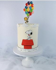 a birthday cake with a snoopy topper and balloons on the top of it