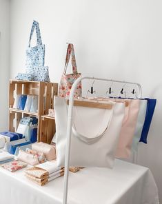 a white table topped with lots of bags and purses next to a shelf filled with books