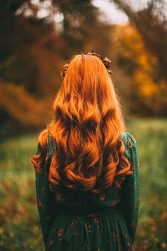 a woman with long red hair standing in a field