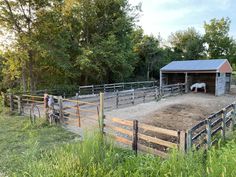 two people are standing in front of a barn with horse pens and fencing around it