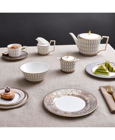 a table topped with plates and cups filled with food on top of a white table cloth