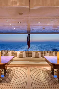 the inside of a boat with couches and tables overlooking the ocean at night time