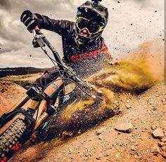 a man riding a dirt bike on top of a dirt field with clouds in the background