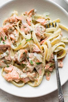 a white plate topped with pasta covered in sauce and salmon on top of it next to a fork