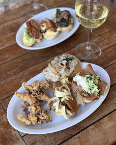 two white plates with food on them next to a glass of wine