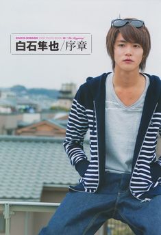 a young man sitting on top of a metal rail next to a roof with buildings in the background