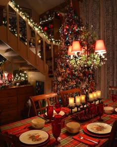 a dining room table set for christmas dinner with lit candles in front of the tree