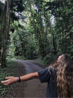 a woman with her arms outstretched on a dirt road surrounded by trees