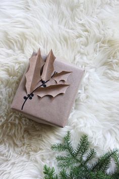 a present wrapped in brown paper on top of a white fur covered floor next to a pine tree