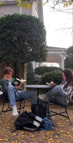 two people sitting at a table in the middle of a courtyard with yellow leaves on the ground