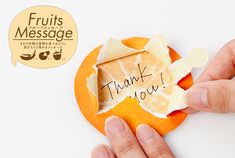 a hand holding a piece of paper with the words thank you written on it and an orange