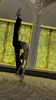 a person doing a handstand in front of a building with lights on it