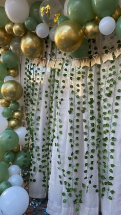 a bunch of balloons and greenery hanging from the ceiling in front of a curtain