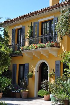 a yellow house with black shutters and flowers on the balconies above it