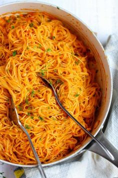 a pan filled with spaghetti and two serving spoons on top of a white towel