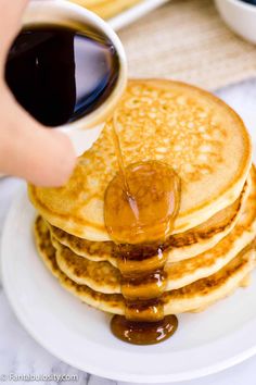 a stack of pancakes with syrup being drizzled over them on a white plate