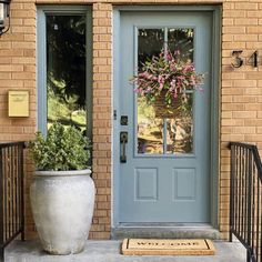 a blue front door with a planter on the steps and a welcome mat in front