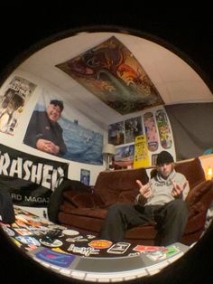 a man sitting on top of a brown couch next to a wall covered in posters