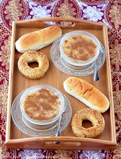 an assortment of breads and pastries in glass dishes on a wooden serving tray