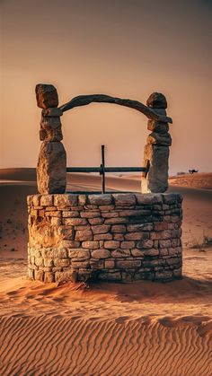 an arch made out of rocks in the middle of sand dunes with a cross on top