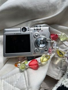 a silver camera sitting on top of a white blanket covered in beads and glass beads