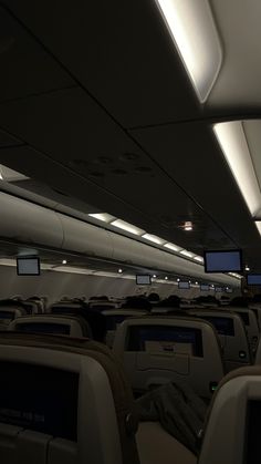 the interior of an airplane with many empty seats and television screens on the wall above them