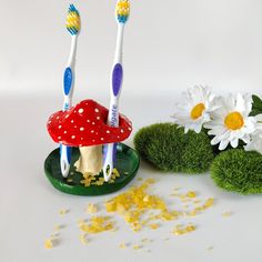 two toothbrushes sitting on top of a green plate next to flowers and grass