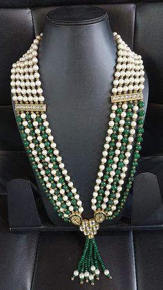 a green and white beaded necklace with tassels on display in a black leather chair