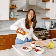 a woman pouring honey into some fruit on a cutting board with bananas and strawberries