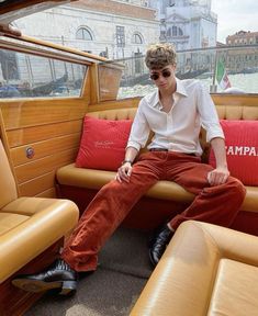 a man sitting on the back of a boat in front of a window with red pillows