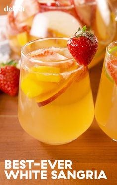 two glasses filled with drinks sitting on top of a wooden table next to strawberries