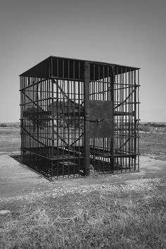 a black and white photo of a caged animal in the middle of an open field