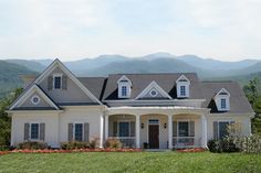 a large white house with mountains in the backgrouds and flowers on the front lawn